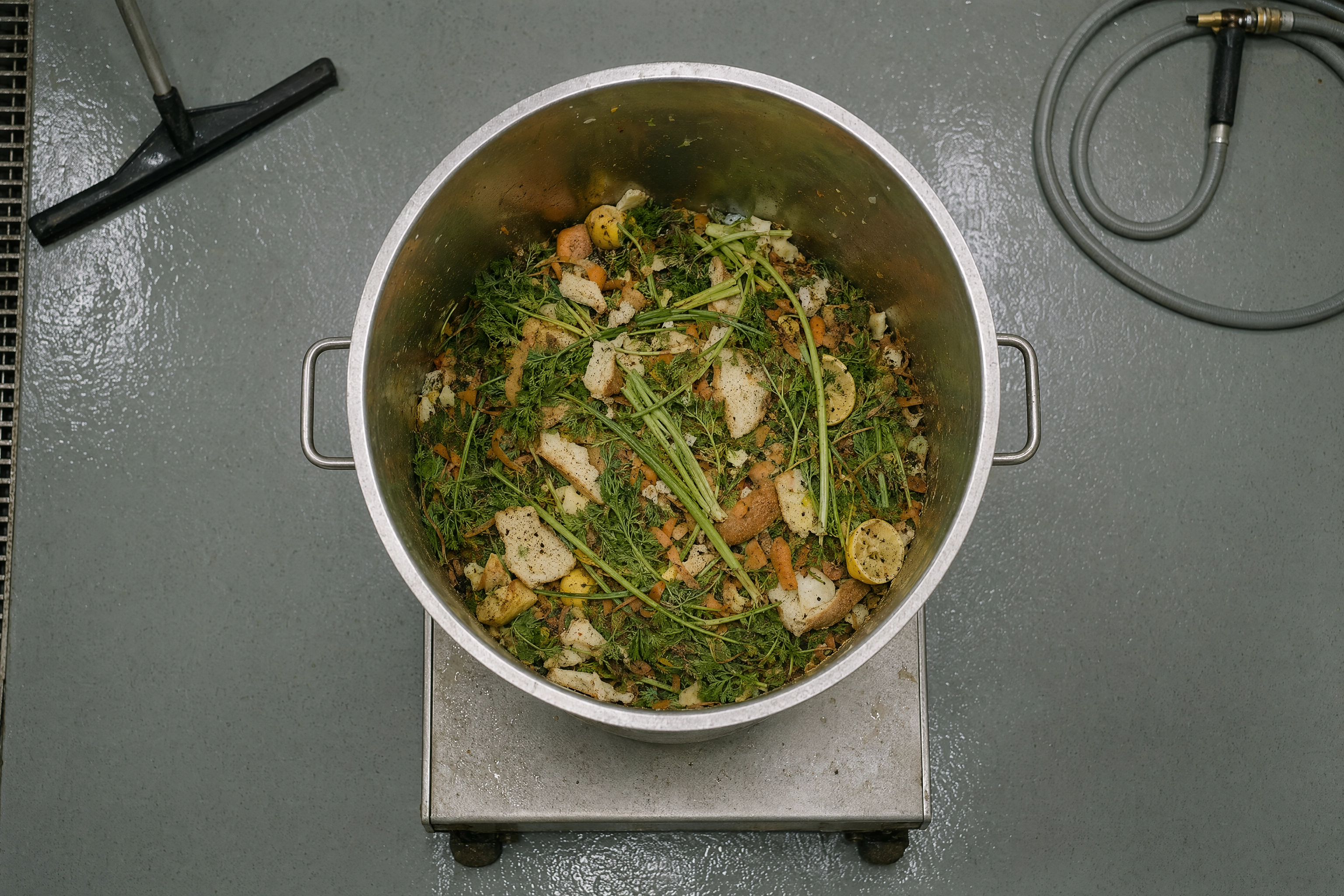 Overhead view of a stainless kitchen bin of food waste on a platform scale, what AI waste-tracking cameras measure