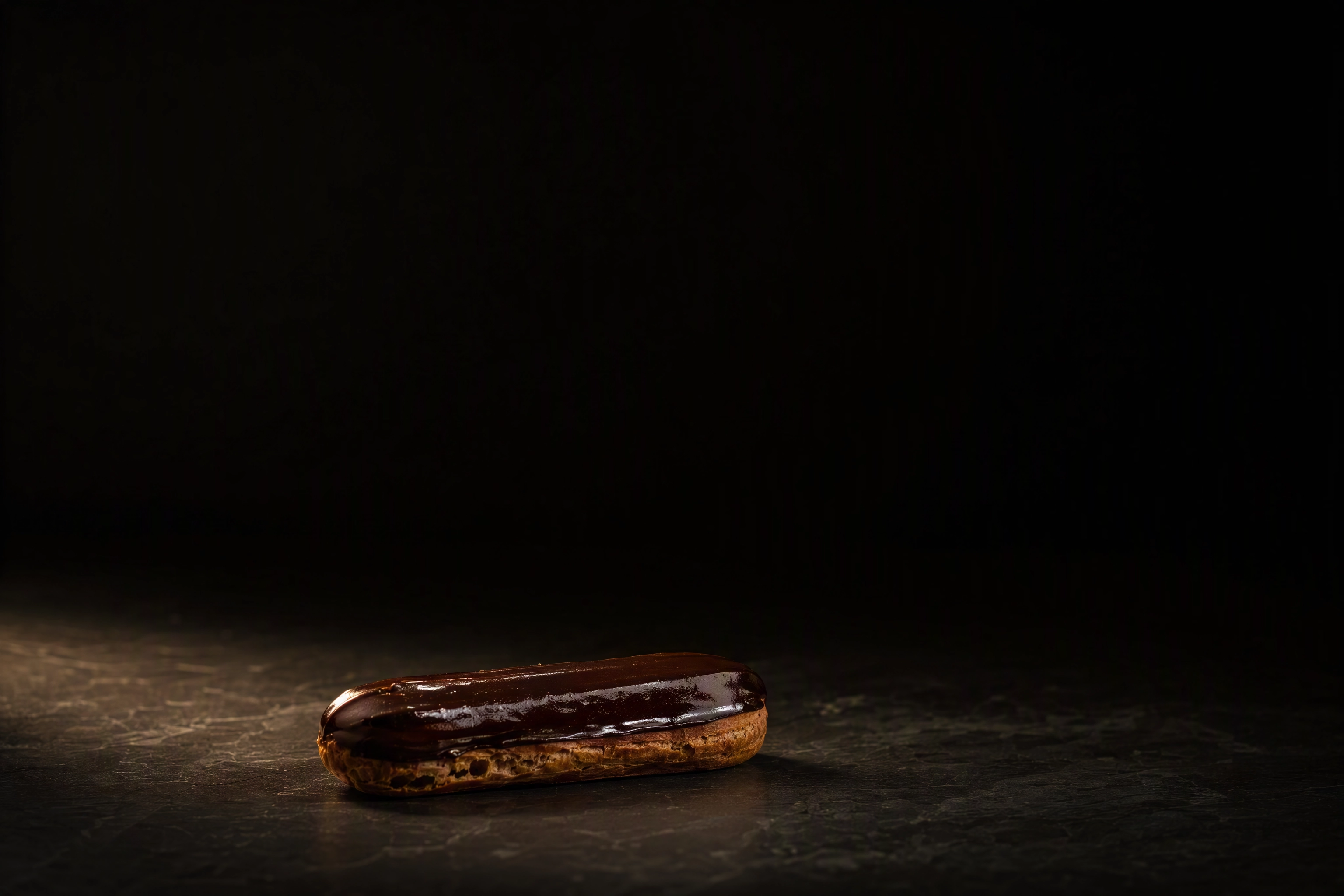 Single eclair placed low in a wide dark frame leaving negative space above for poster headline type