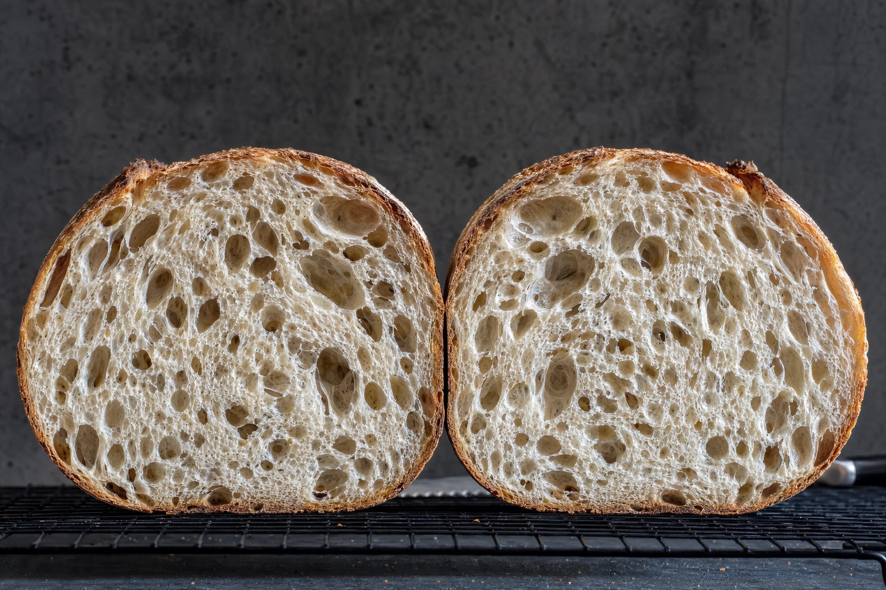 Cross-section crumb shot of a halved sourdough loaf with the cut face square to camera under skimming light