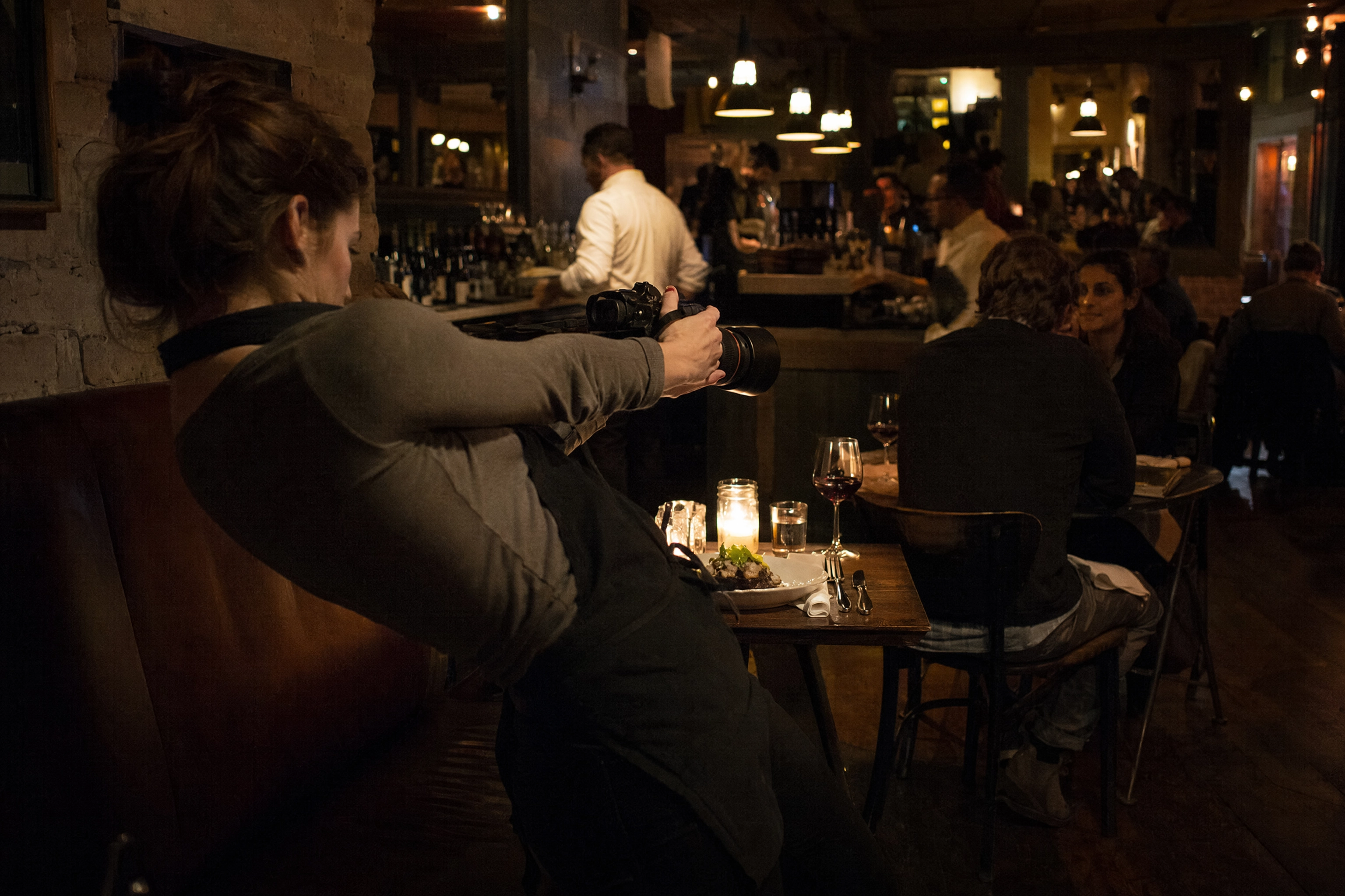 Photographer leaning back awkwardly at a cramped restaurant two-top trying to fit a plate in frame with a long lens