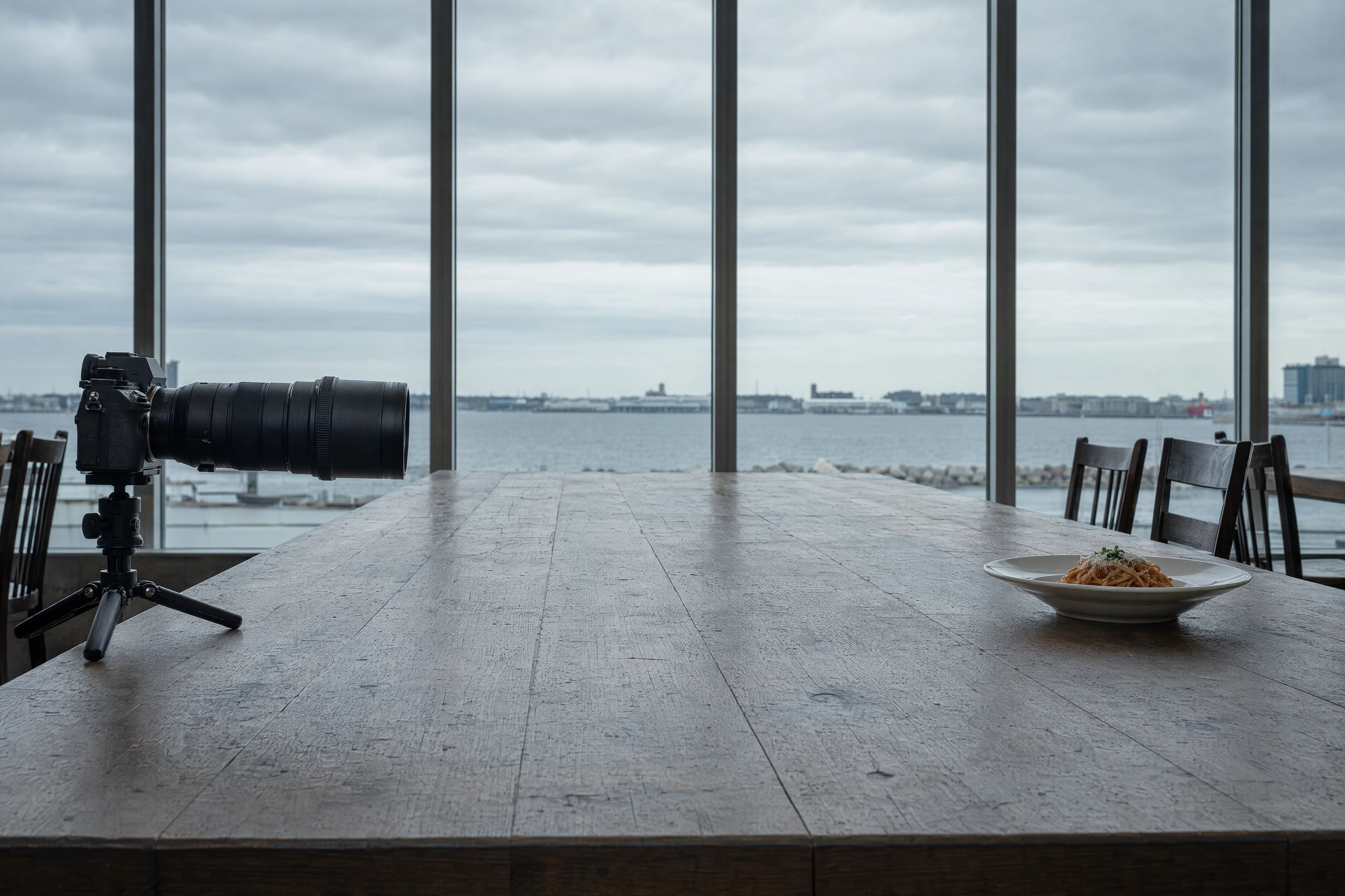 Camera on a tripod positioned far down a long table from a small plate, showing telephoto lens working distance