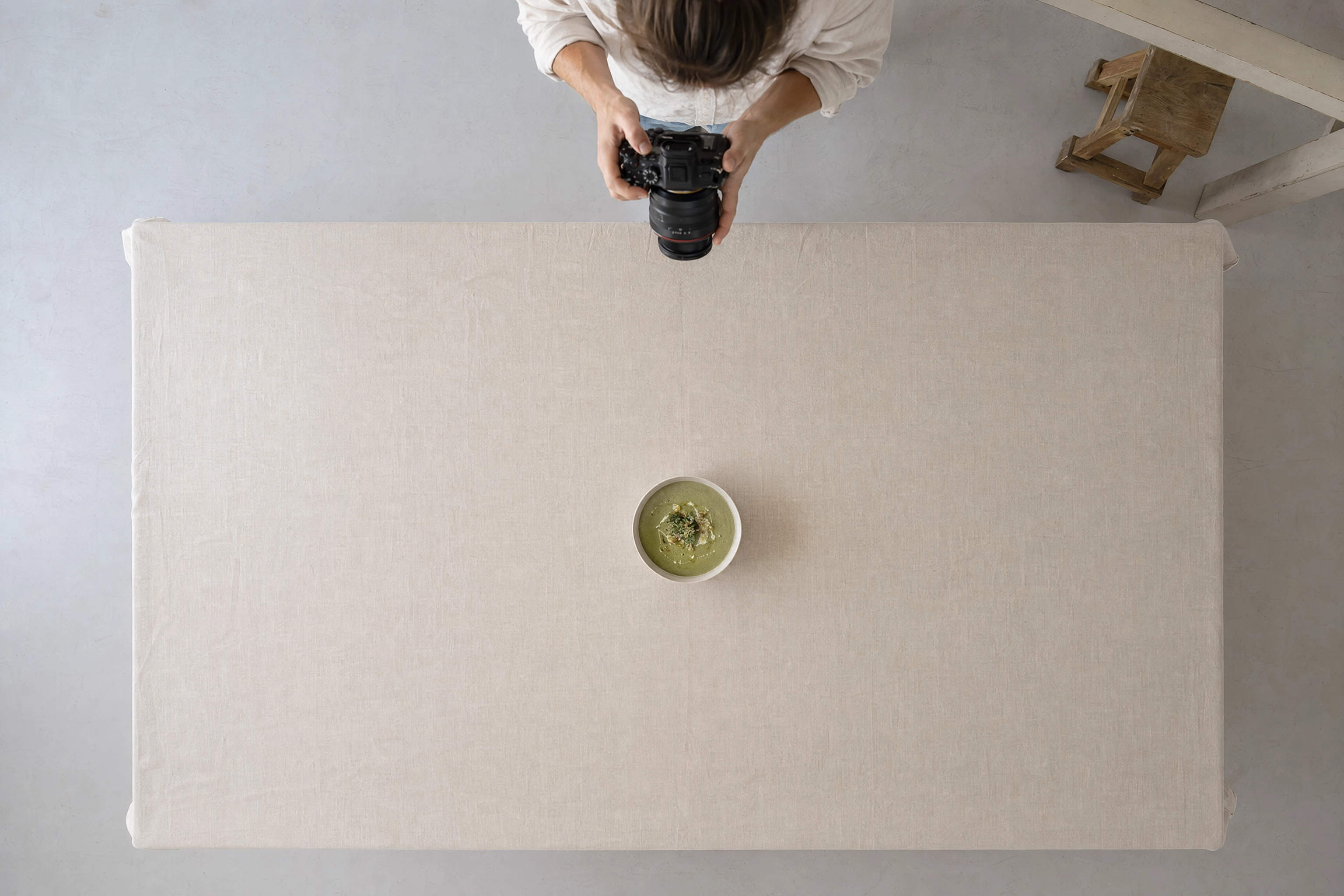 Overhead flat-lay of a single soup bowl on linen with arms reaching down, showing camera height needed for flat lays