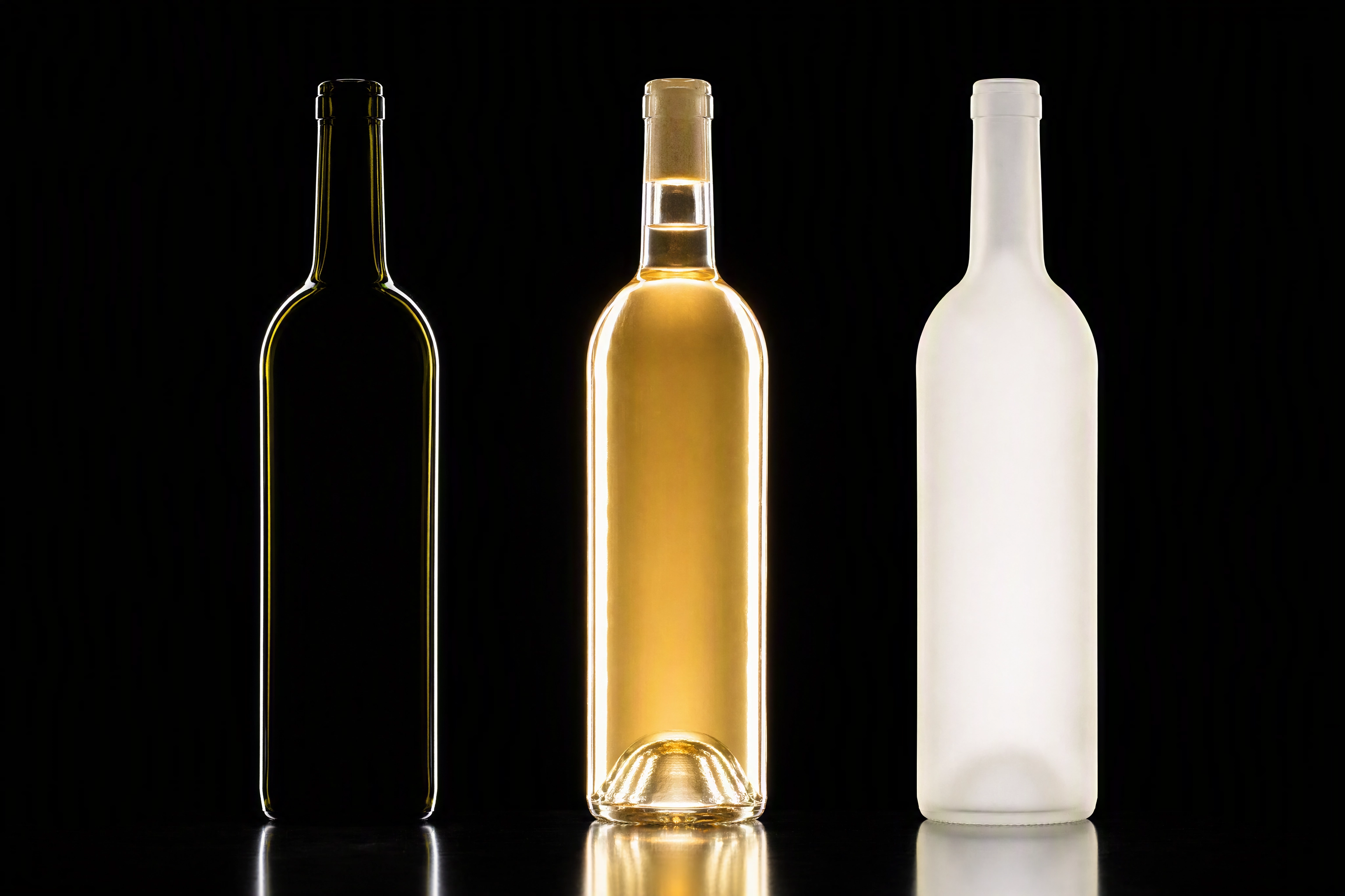 Dark green, clear and frosted bottles backlit side by side, showing how glass tint changes bottle photography lighting