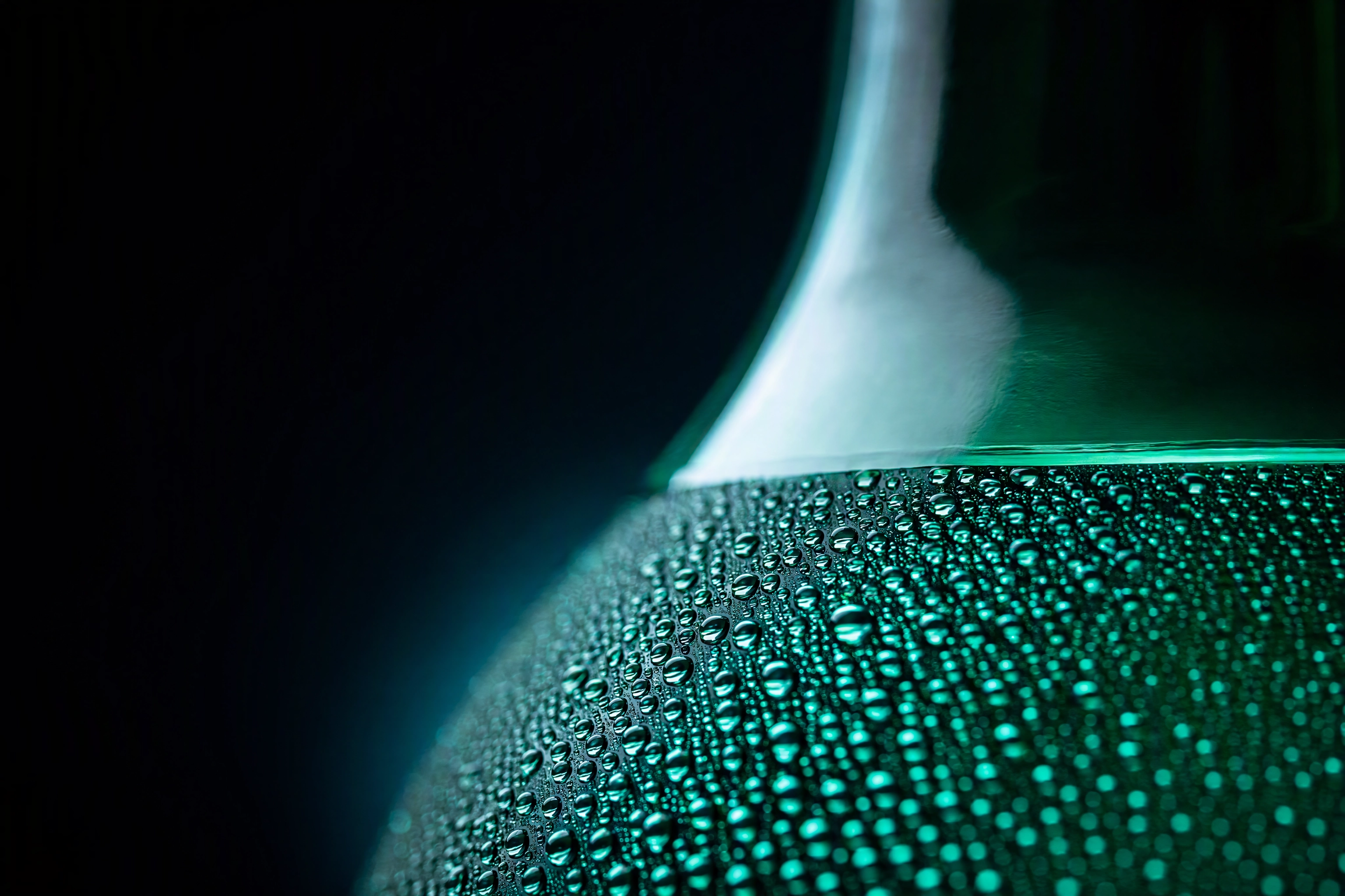 Macro of fake glycerine condensation beads backlit on a chilled green bottle shoulder, stopping at the fill line