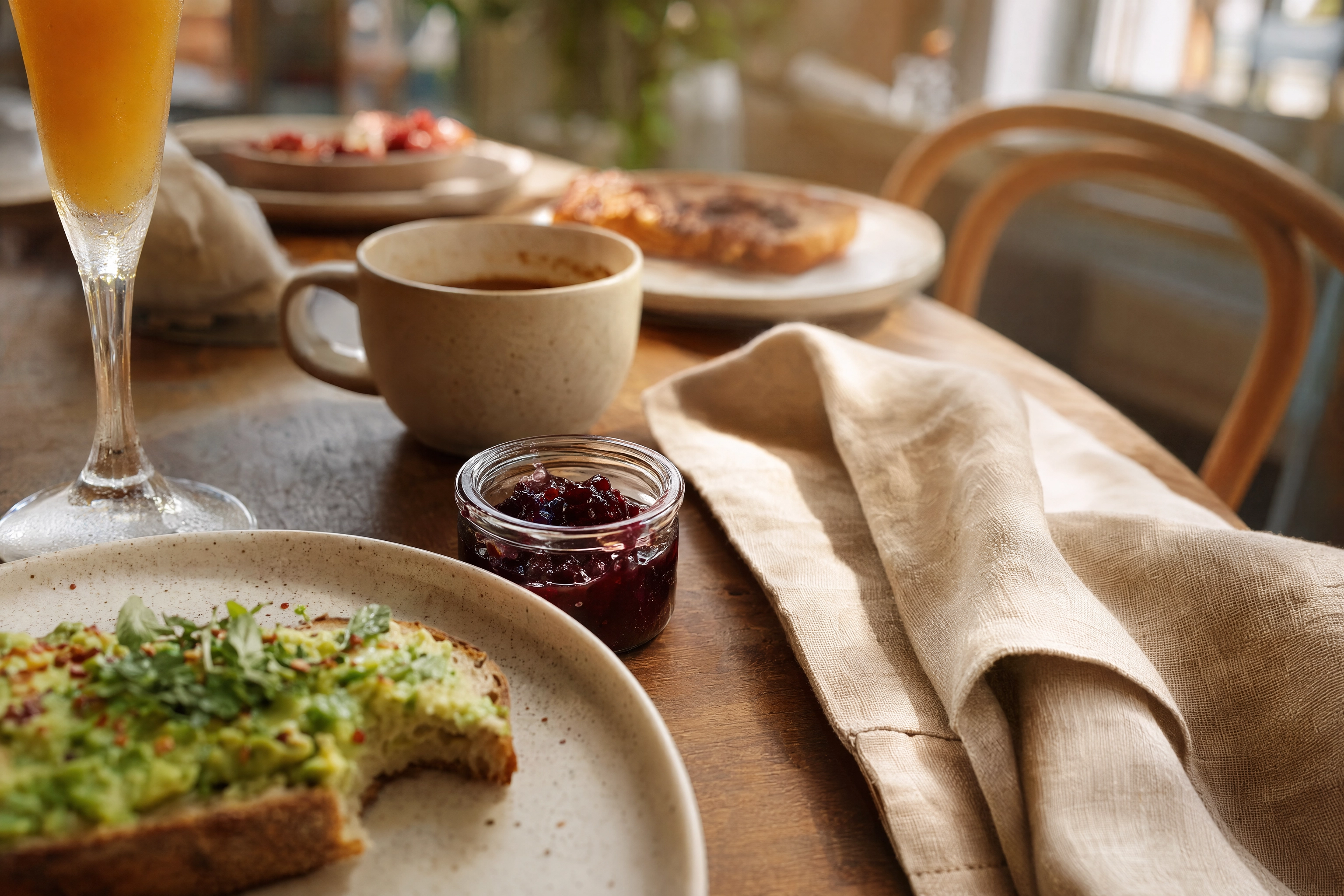 Table-level corner crop of a brunch spread with a half-eaten plate and pushed-out chair implying a shared table