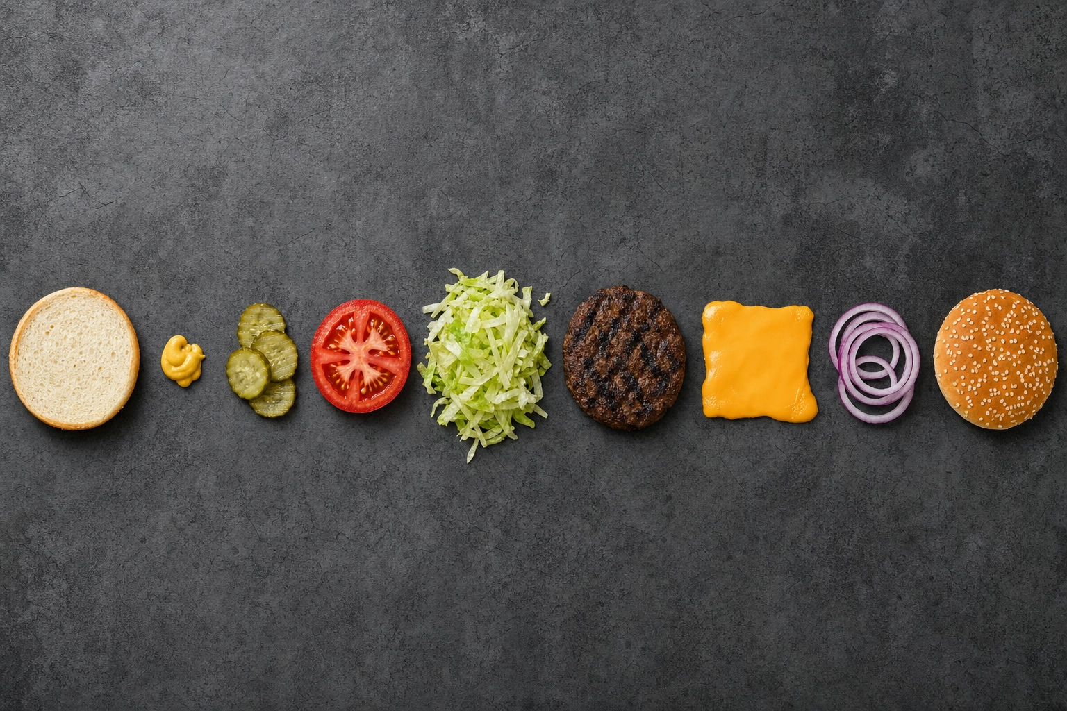 Overhead flat-lay deconstructed cheeseburger with ingredients spread in build order on concrete surface