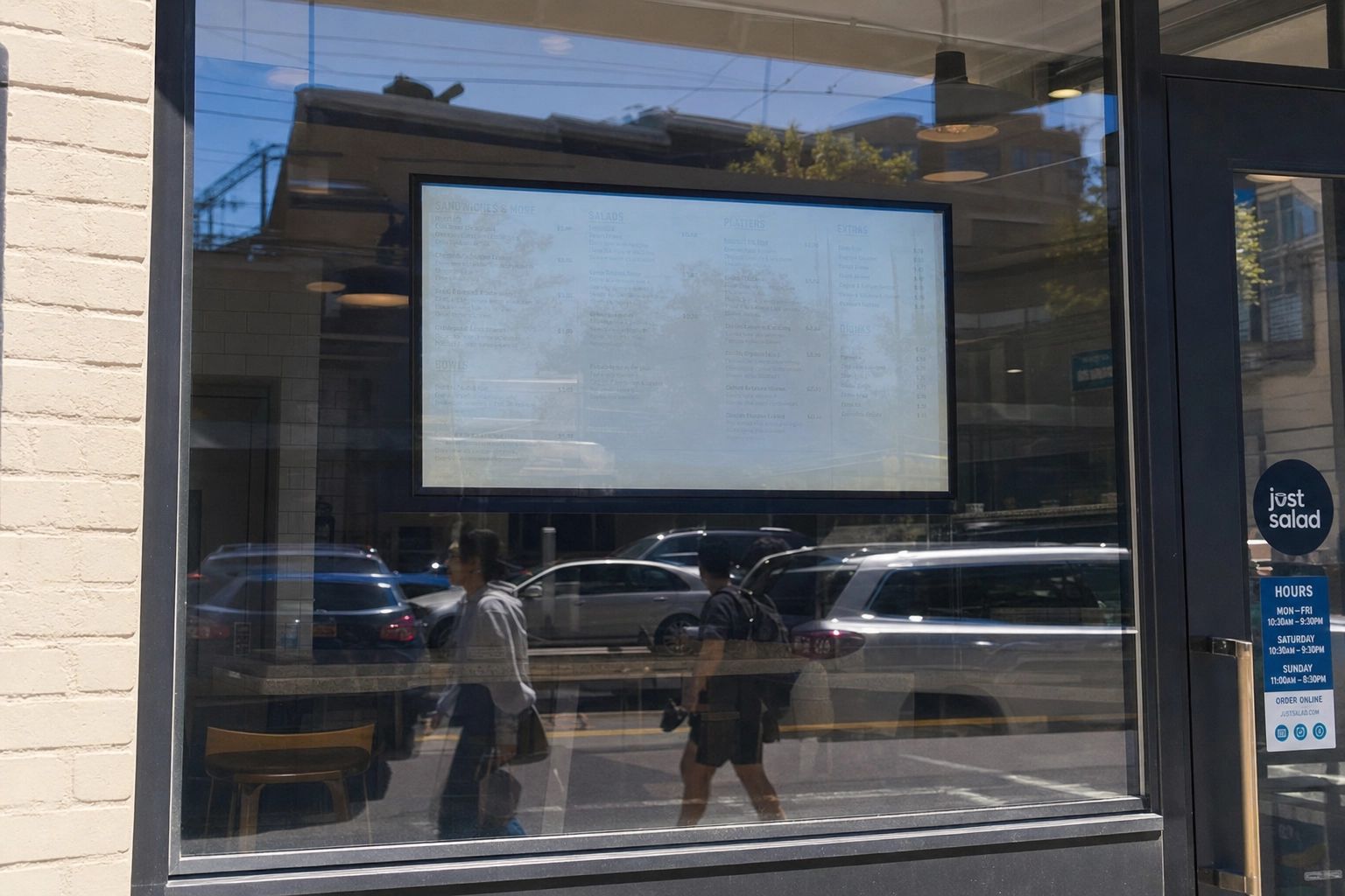 Digital menu board washed out by sun glare behind a storefront window, showing a common brightness mistake