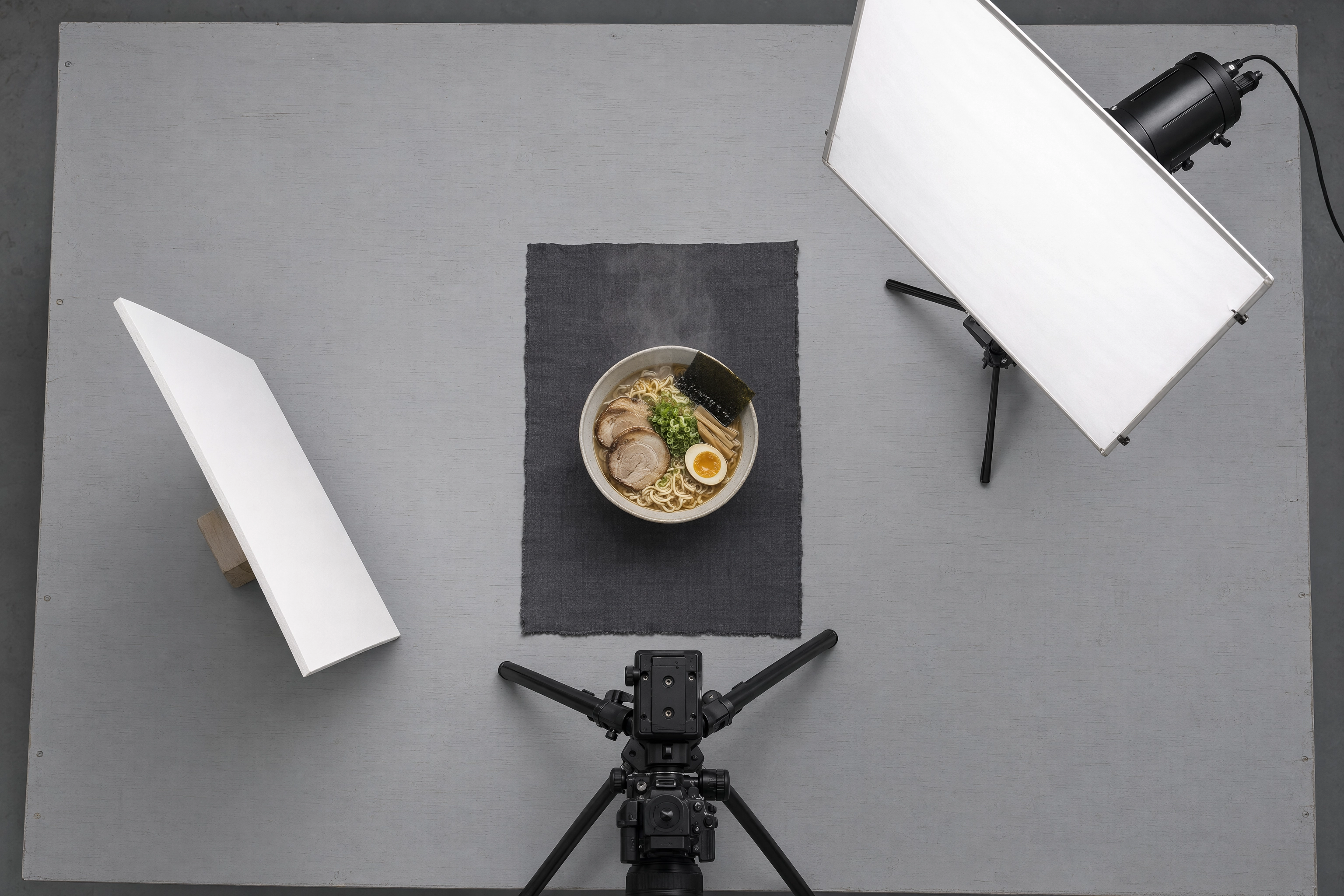 Overhead view of a two-light food photography setup showing diffusion panel, bounce card, tripod and a bowl of ramen