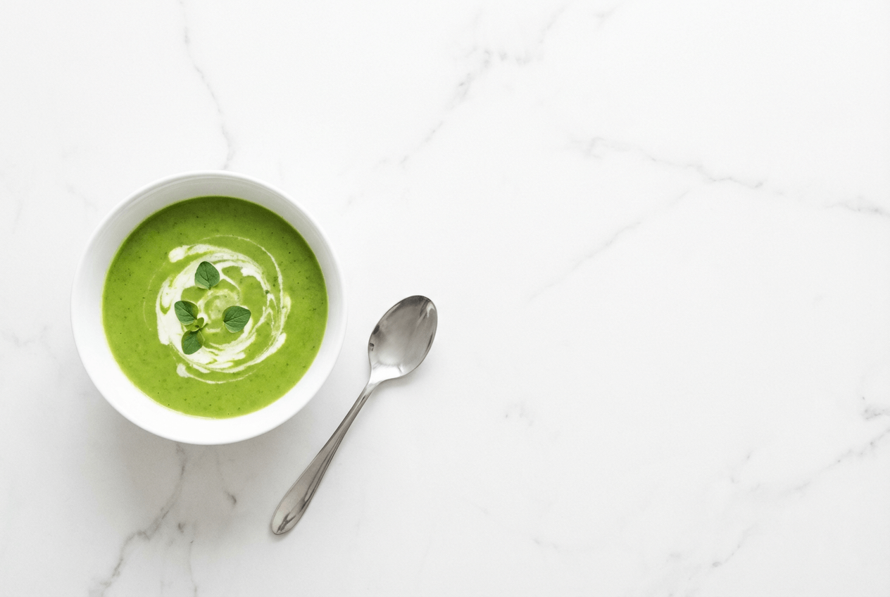 Composición minimalista de fotografía de comida con espacio negativo mostrando un bol de sopa de guisantes sobre mármol blanco