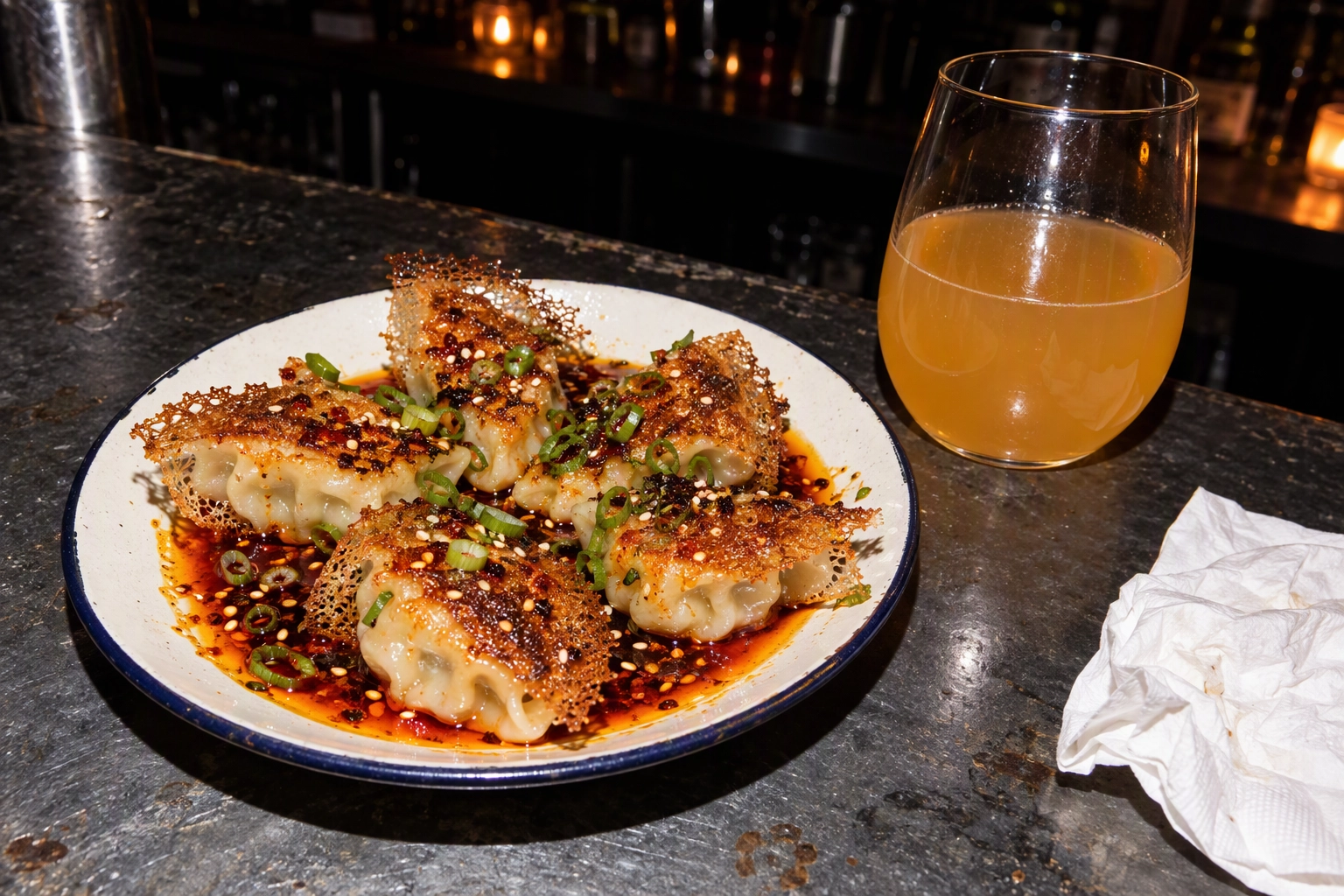 Pan-fried dumplings with chili oil and a glass of orange wine shot with direct on-camera flash at a late-night bar counter