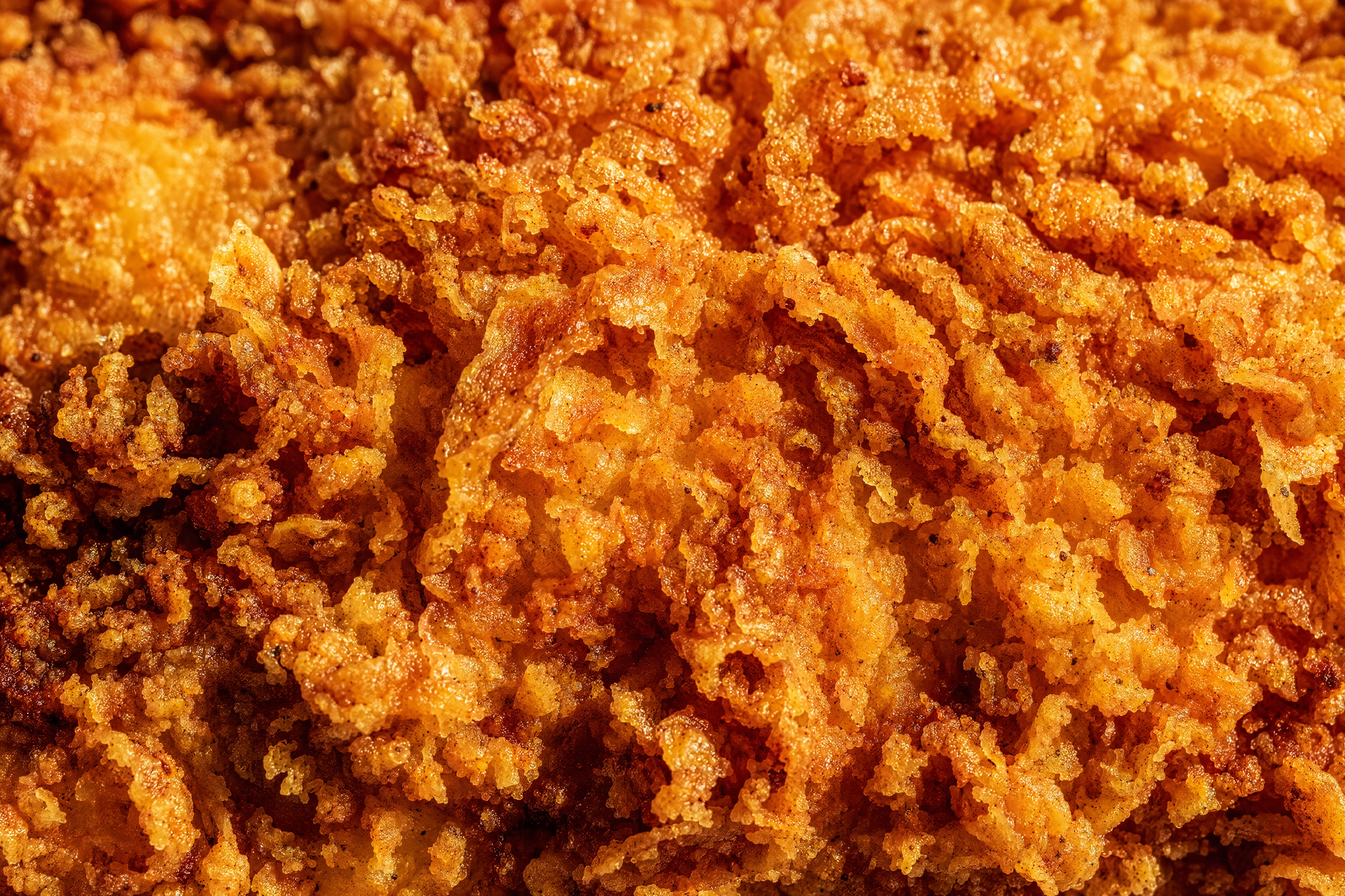 Extreme macro of shatter-crisp golden fried chicken crust with raking light revealing every craggy ridge and air pocket