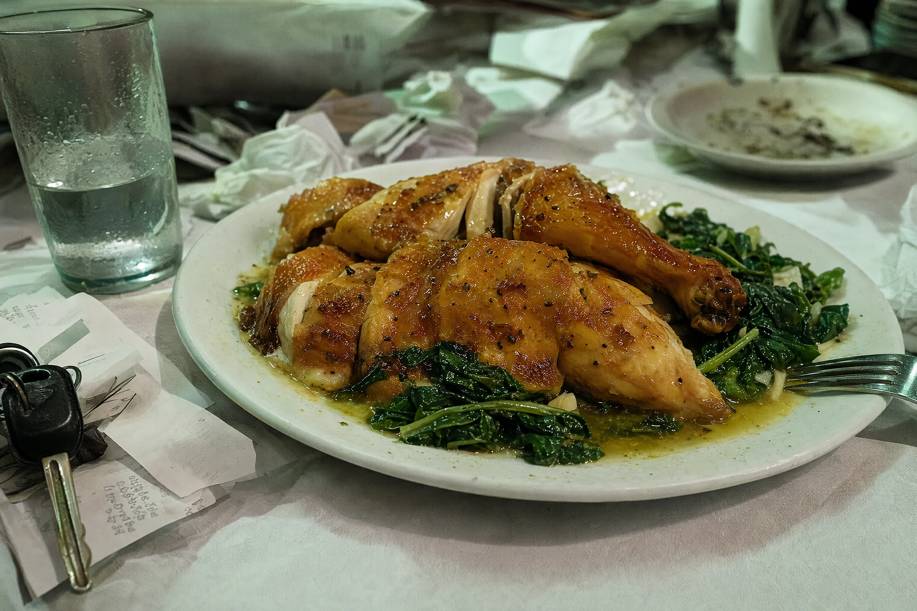 Beautifully roasted chicken plate surrounded by receipts, keys and a water glass under green overhead light, the cluttered background that gets photos rejected