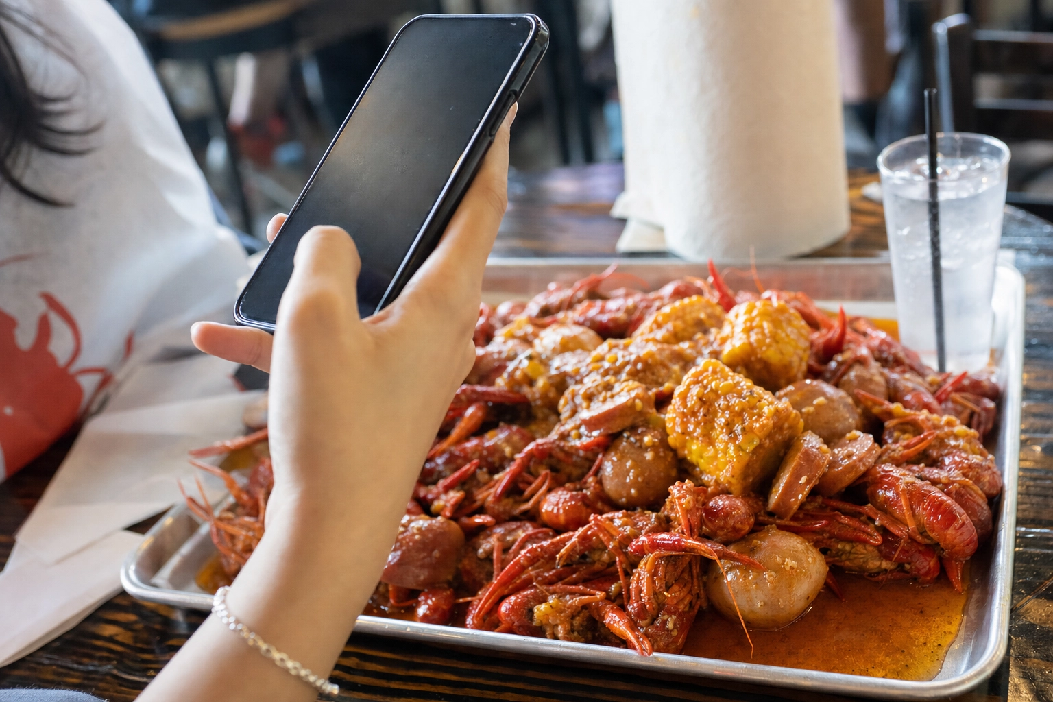Hand using a smartphone to photograph a Viet-Cajun crawfish boil tray at a Houston seafood restaurant table