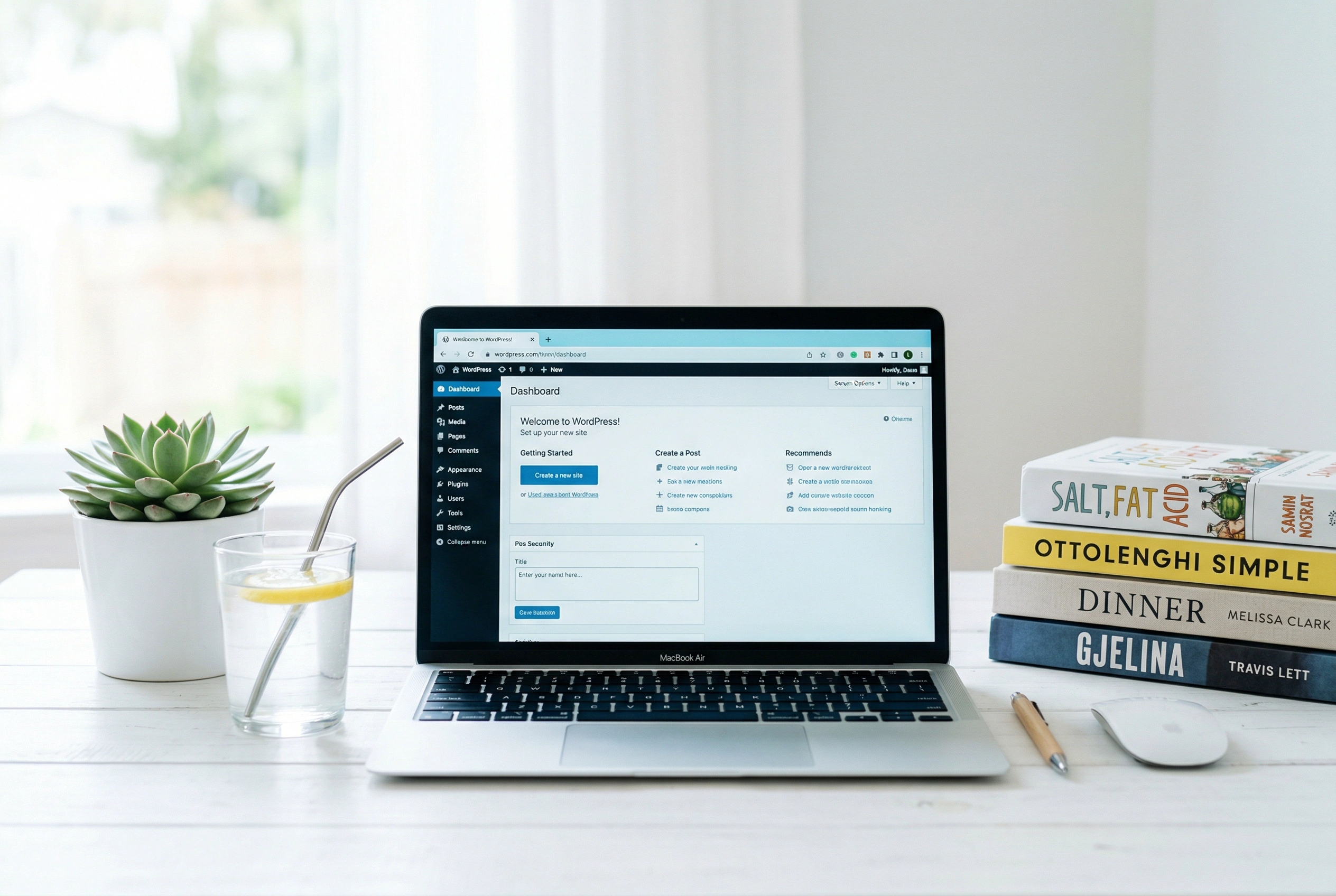 Clean minimal desk setup with laptop showing blog dashboard alongside cookbooks and succulent plant