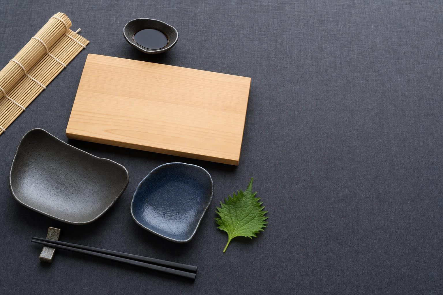 Japanese tableware styling flat-lay with hinoki board, ceramic dishes, tapered chopsticks and shiso on dark linen