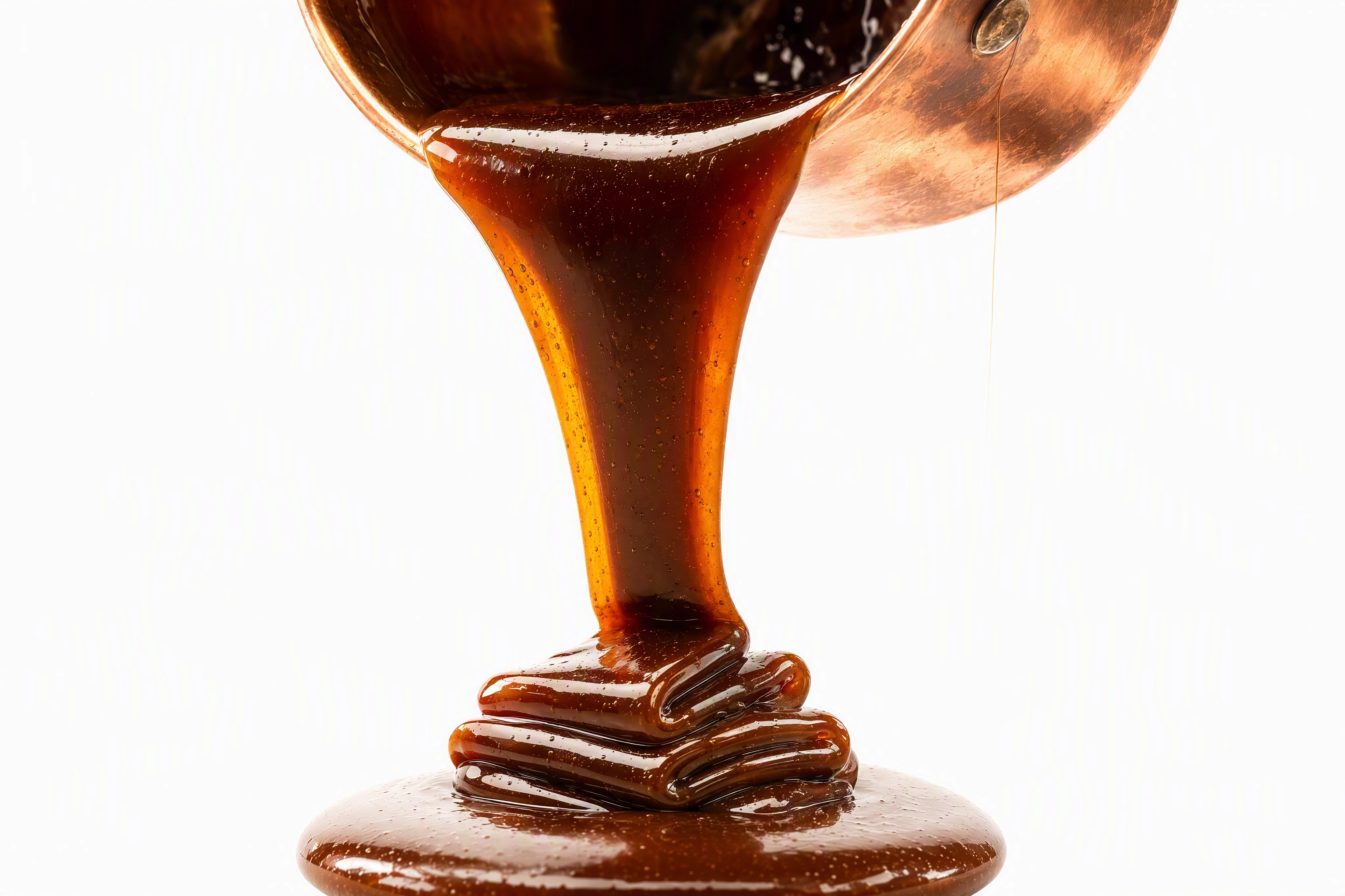 Backlit macro of a thick caramel ribbon pouring and folding, showing sauce viscosity in close-up food photography