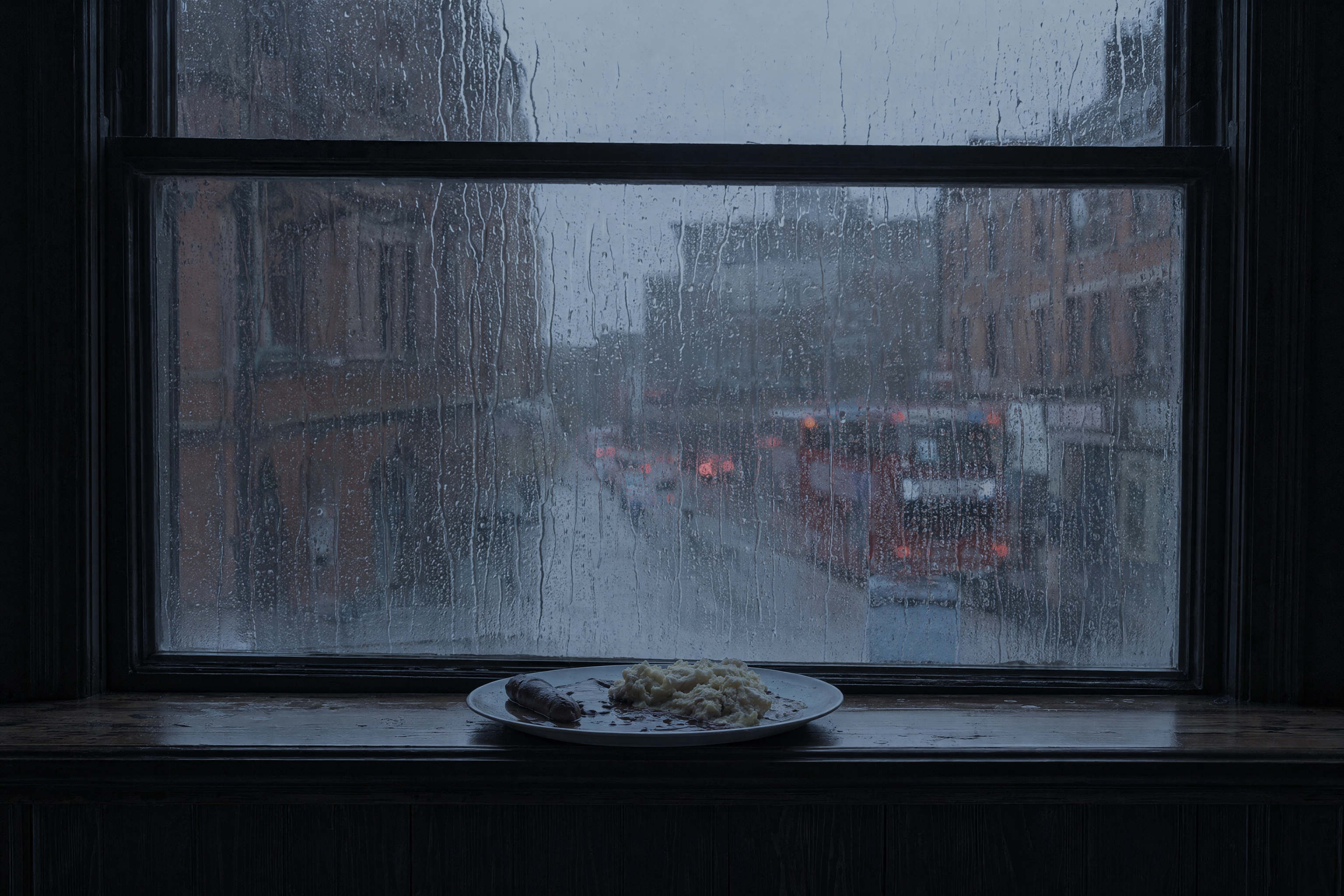 Rain running down a Manchester bar window in December with a plate on the sill drained of colour by dim daylight