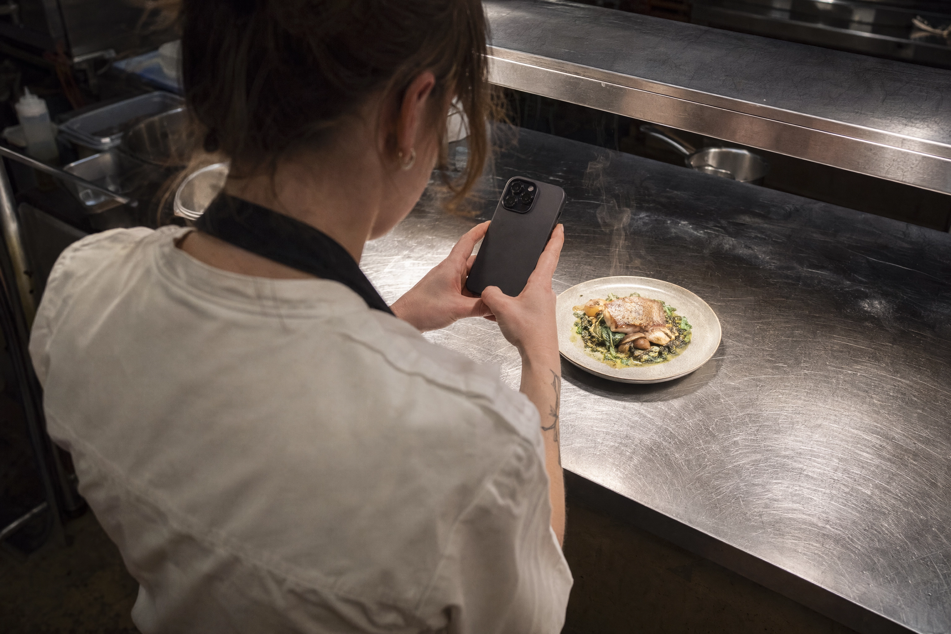Cafe staff photographing a plated dish on a phone, the everyday input for AI food photography between shoots