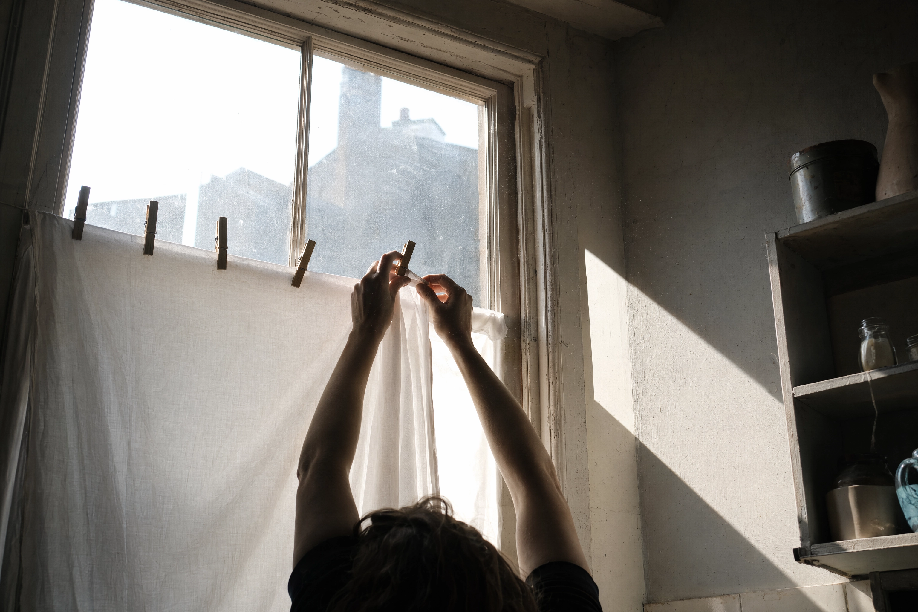 Arms clipping a plain white bedsheet across a window to diffuse hard sun for food photography