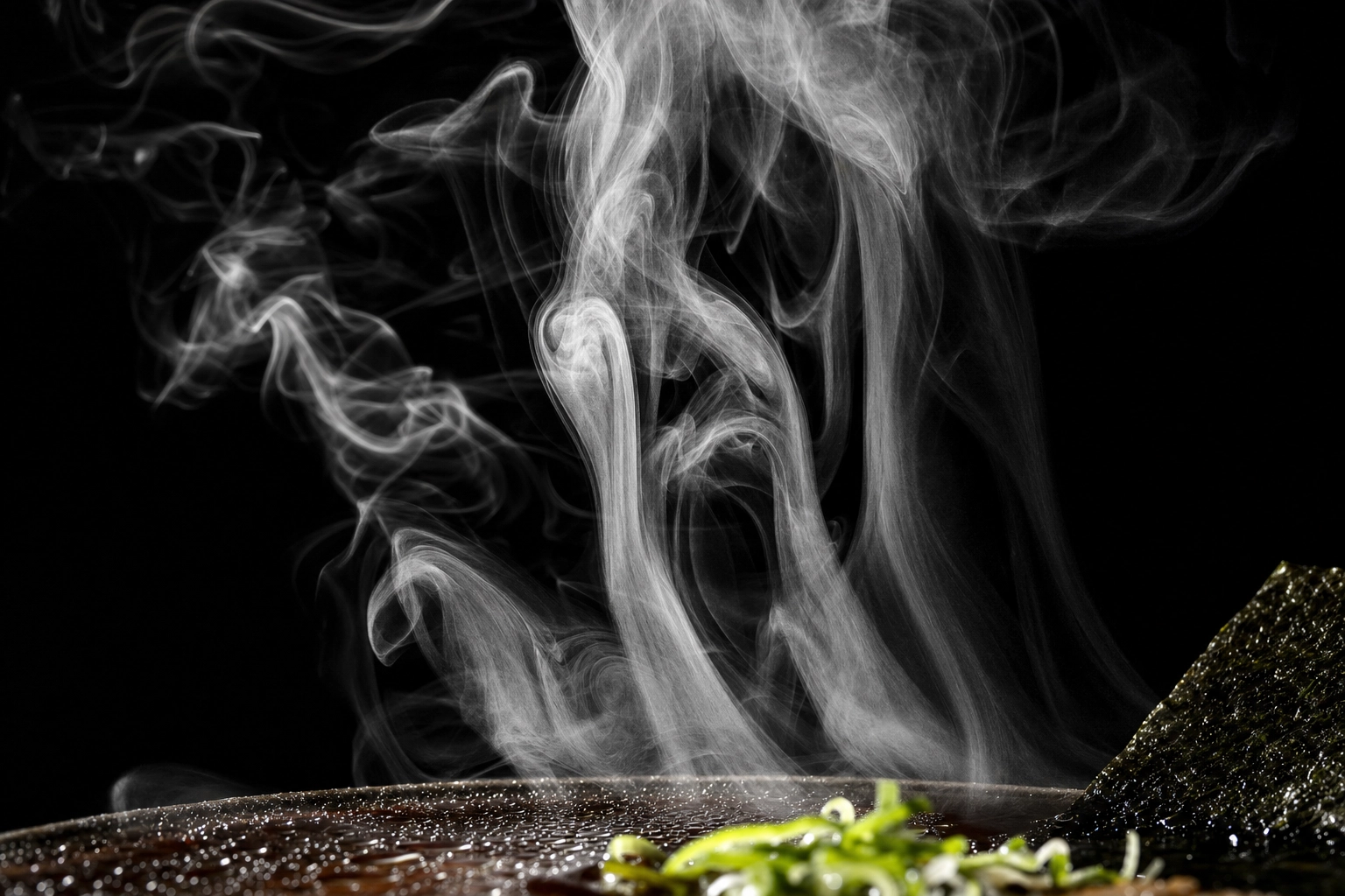 Backlit steam wisps rising from dark ramen broth against a black background
