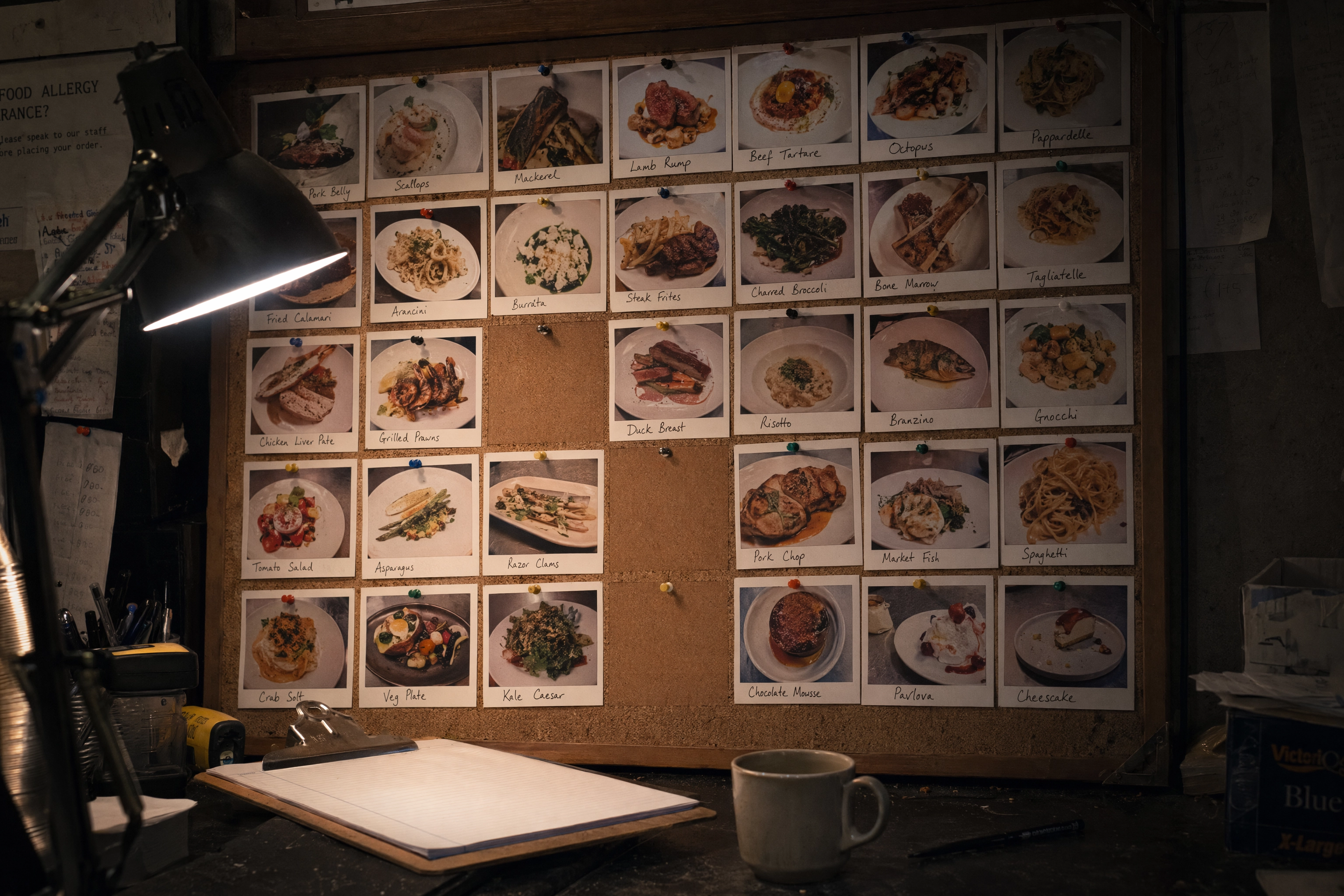 Back-office corkboard of printed dish photos with empty gaps where new specials are missing