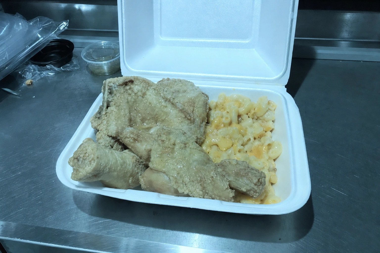 Pale flat fried chicken and mac in a styrofoam takeout box under harsh fluorescent light, a bad soul food photo