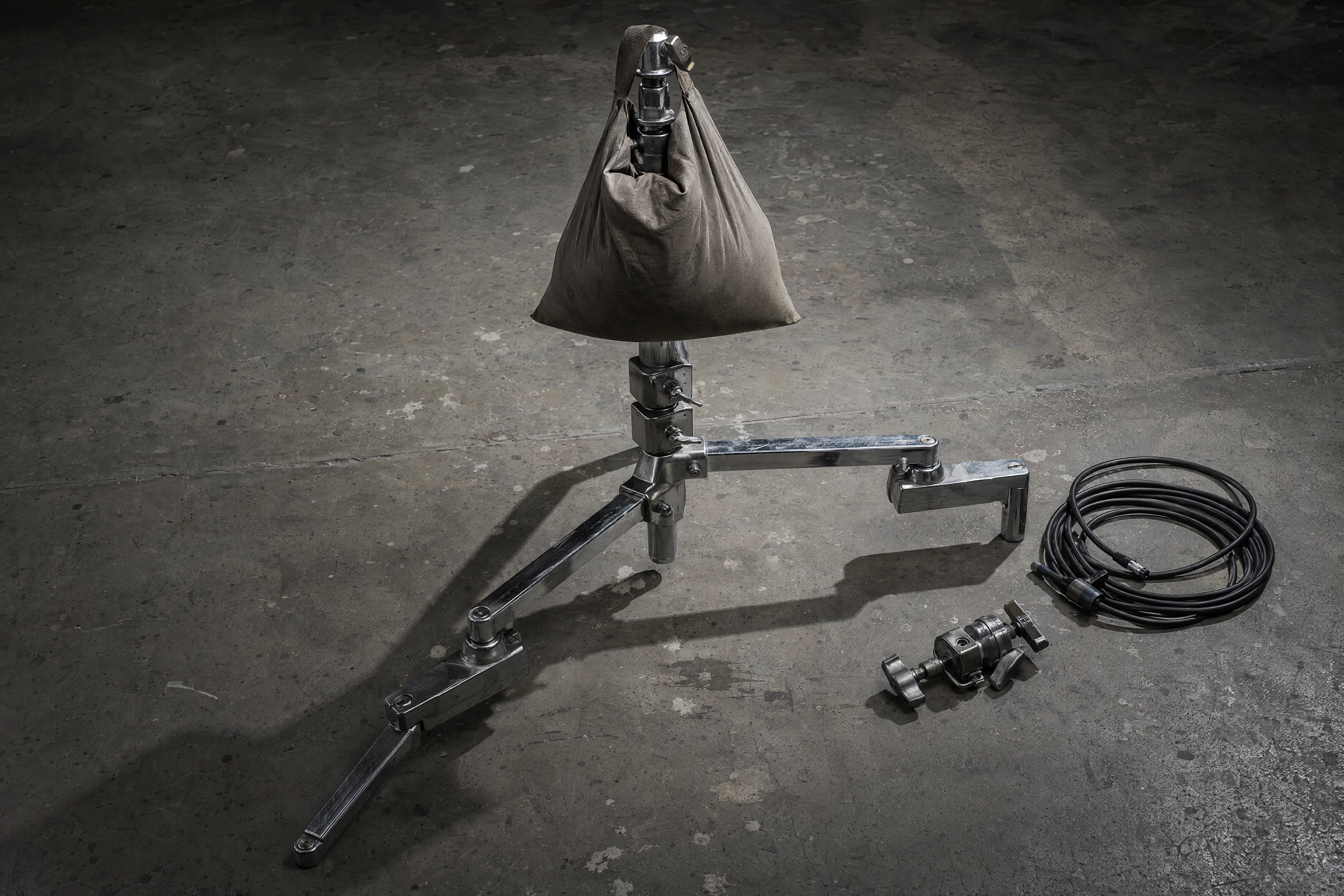 Chrome C-stand base with offset stacked legs and a sandbag weighting it down for overhead camera work