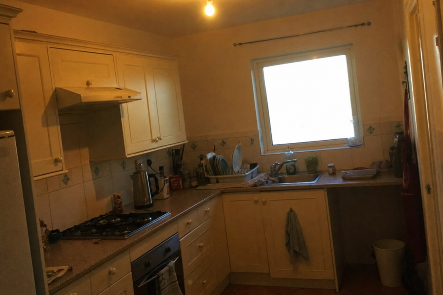 Dim, yellow-tinted smartphone photo of an Airbnb kitchen before editing, underexposed with a blown-out window