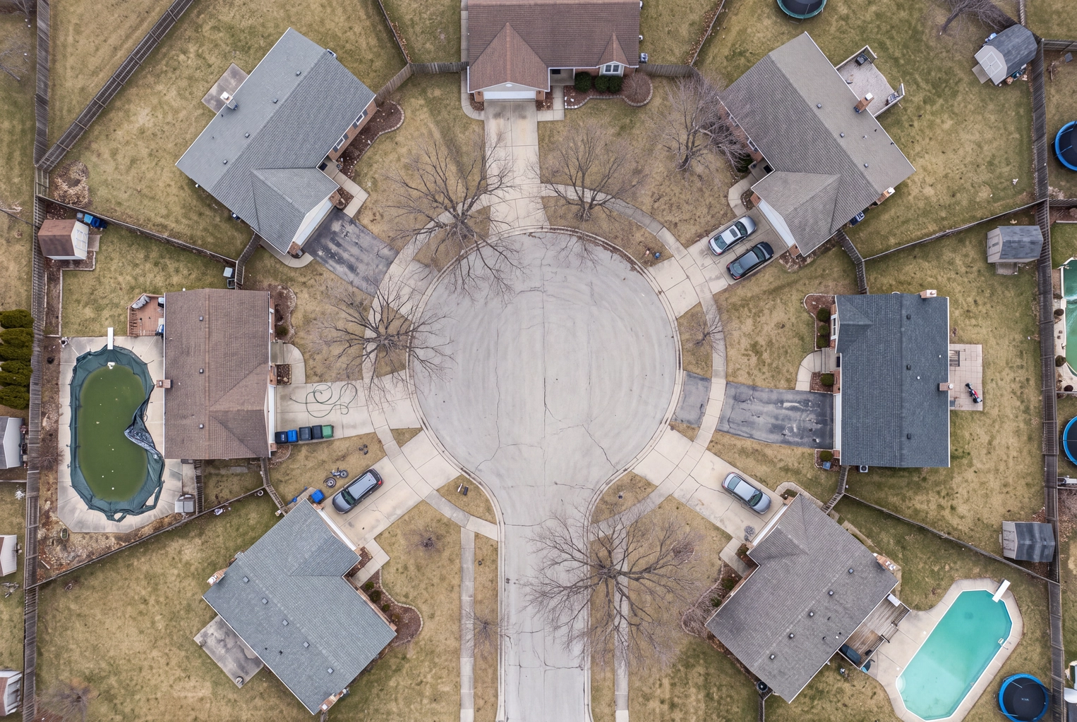 Aerial view of a cul-de-sac with brown lawns, a green covered pool and a clear one, the listing photo fixes AI editors handle