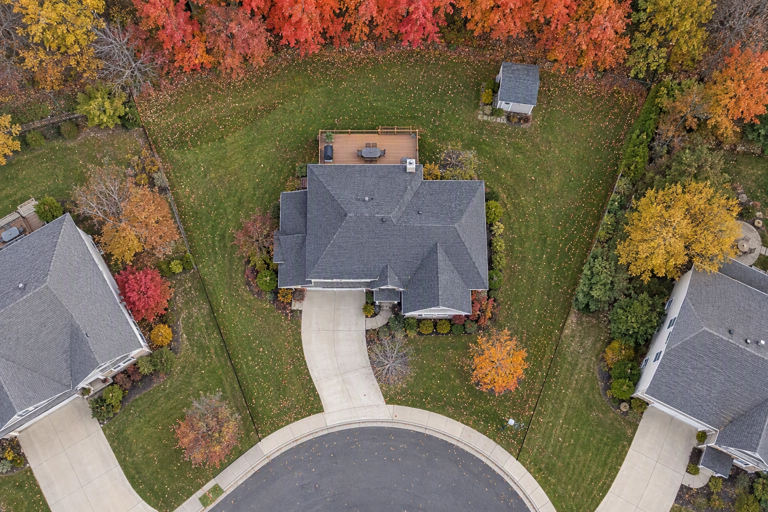 Top-down drone photo of a pie-shaped cul-de-sac lot in autumn showing roof, deck, shed and wooded rear boundary
