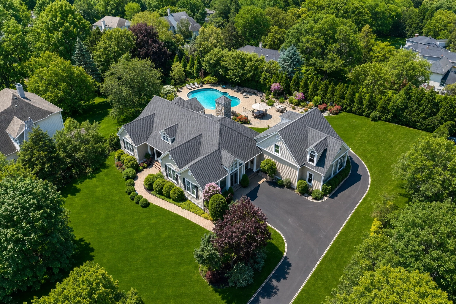 Aerial drone still of a suburban property showing the roof, blue pool, patio, and green backyard from above