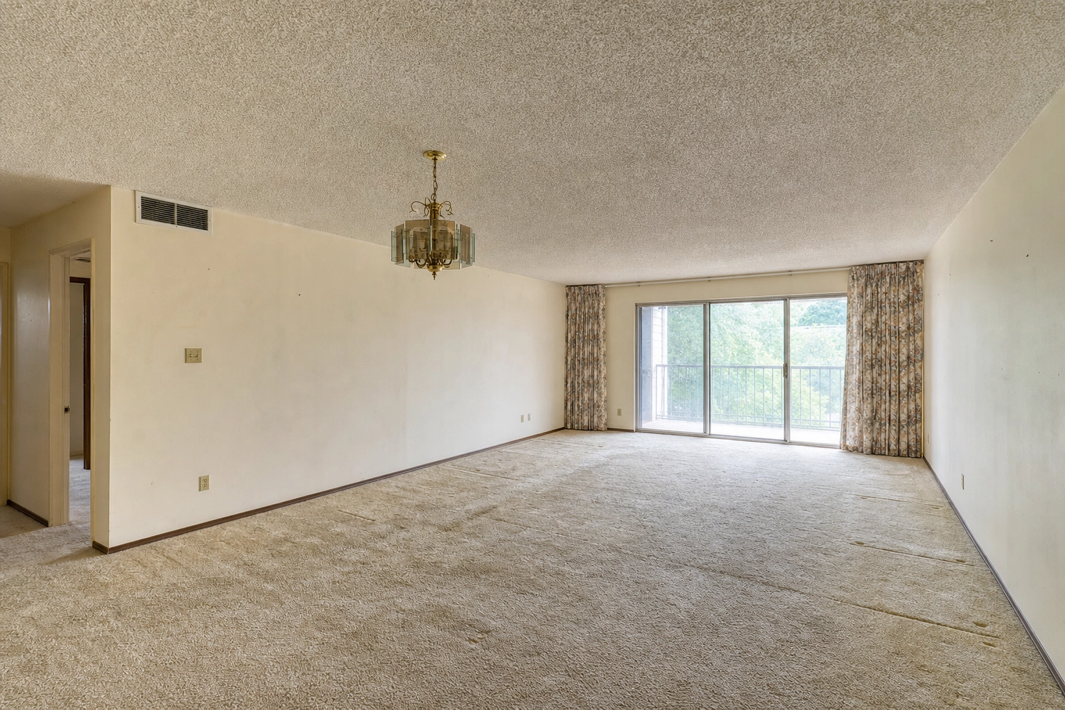 Vacant dated 1980s living room with worn carpet and brass fixtures, a prime virtual staging candidate