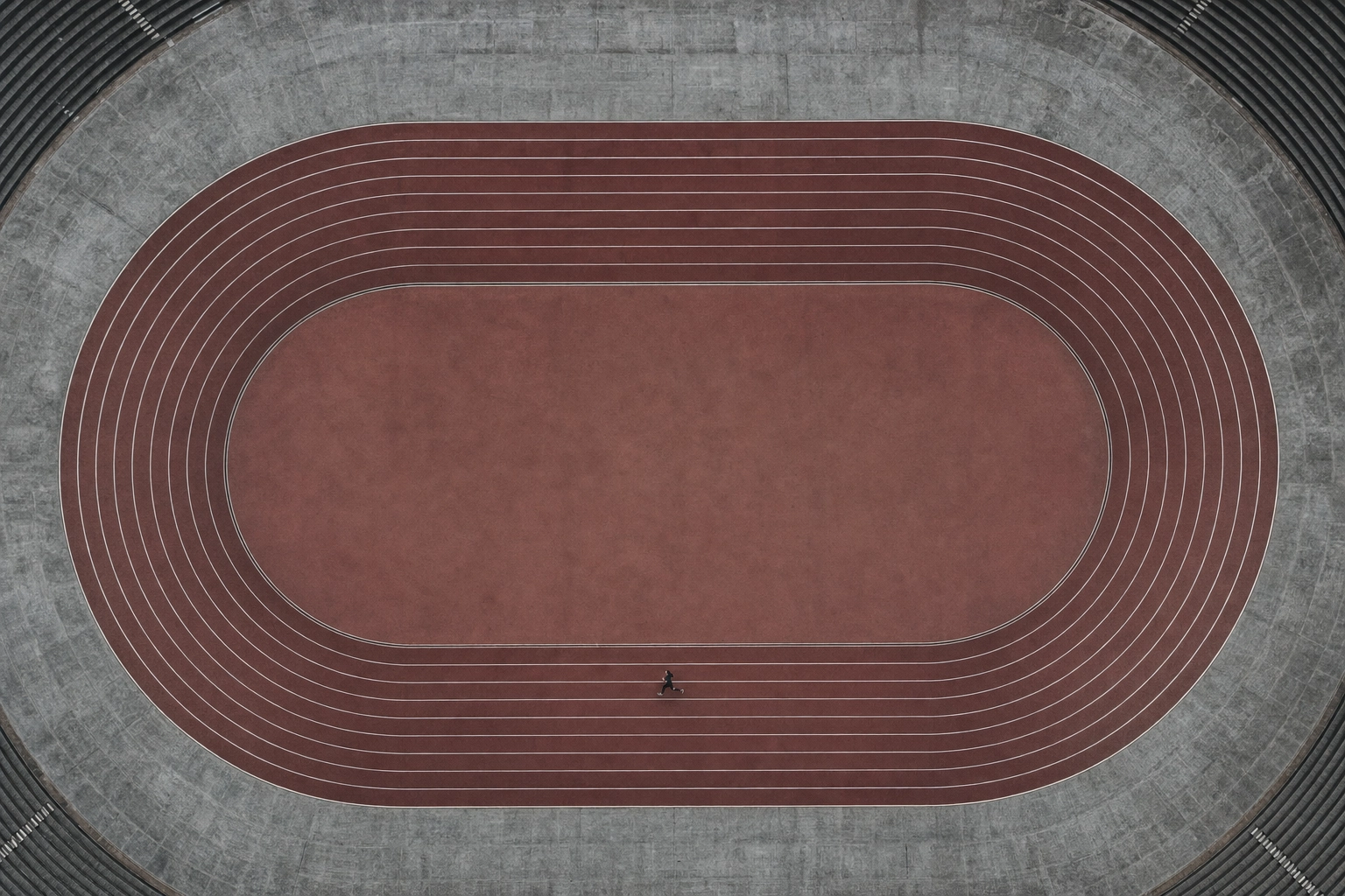 Aerial view of a lone runner on a looping red running track, a metaphor for repetitive scripted speaking scenarios