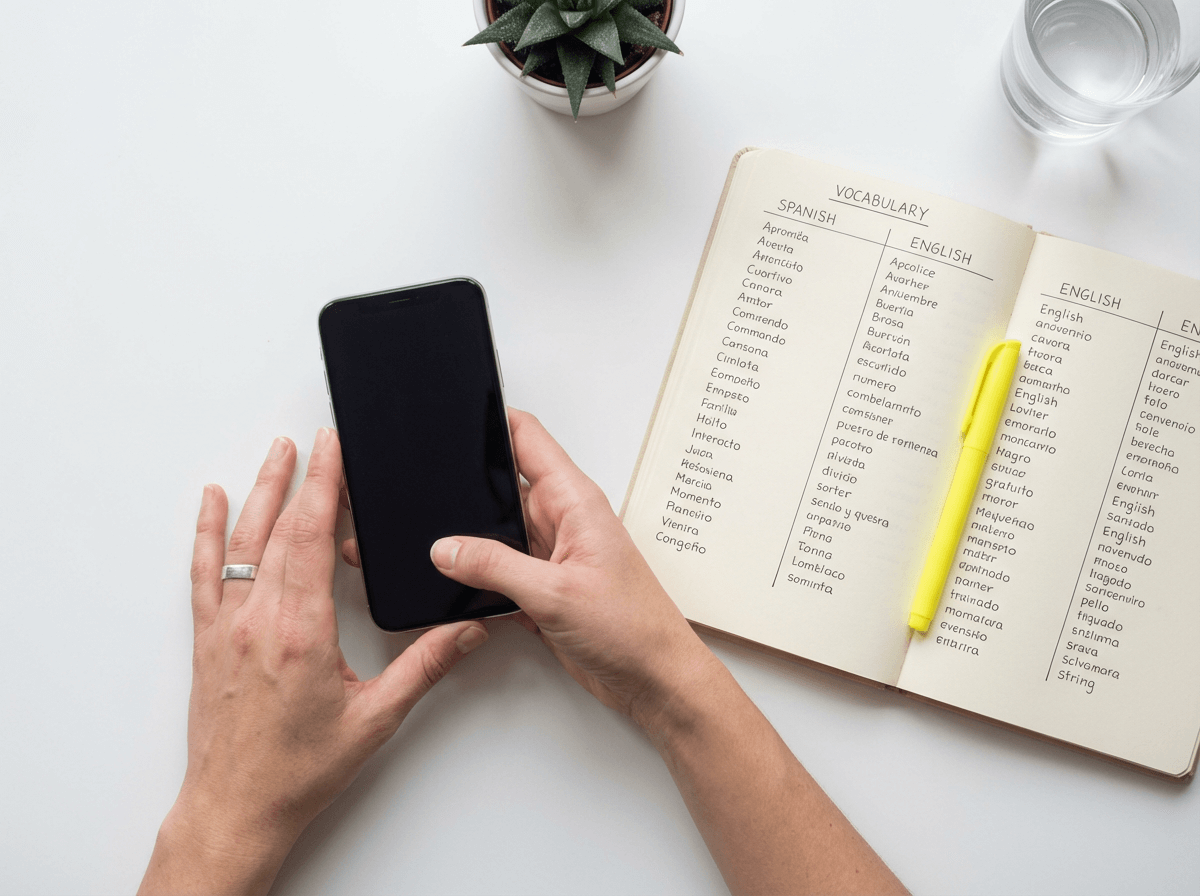 Hands holding smartphone with vocabulary notebook showing structured English learning approach