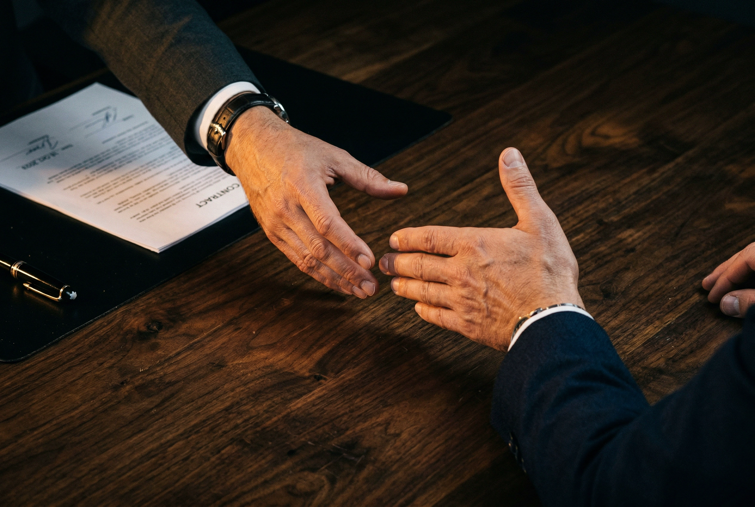 Close-up of hands reaching across desk during business negotiation deal-making moment
