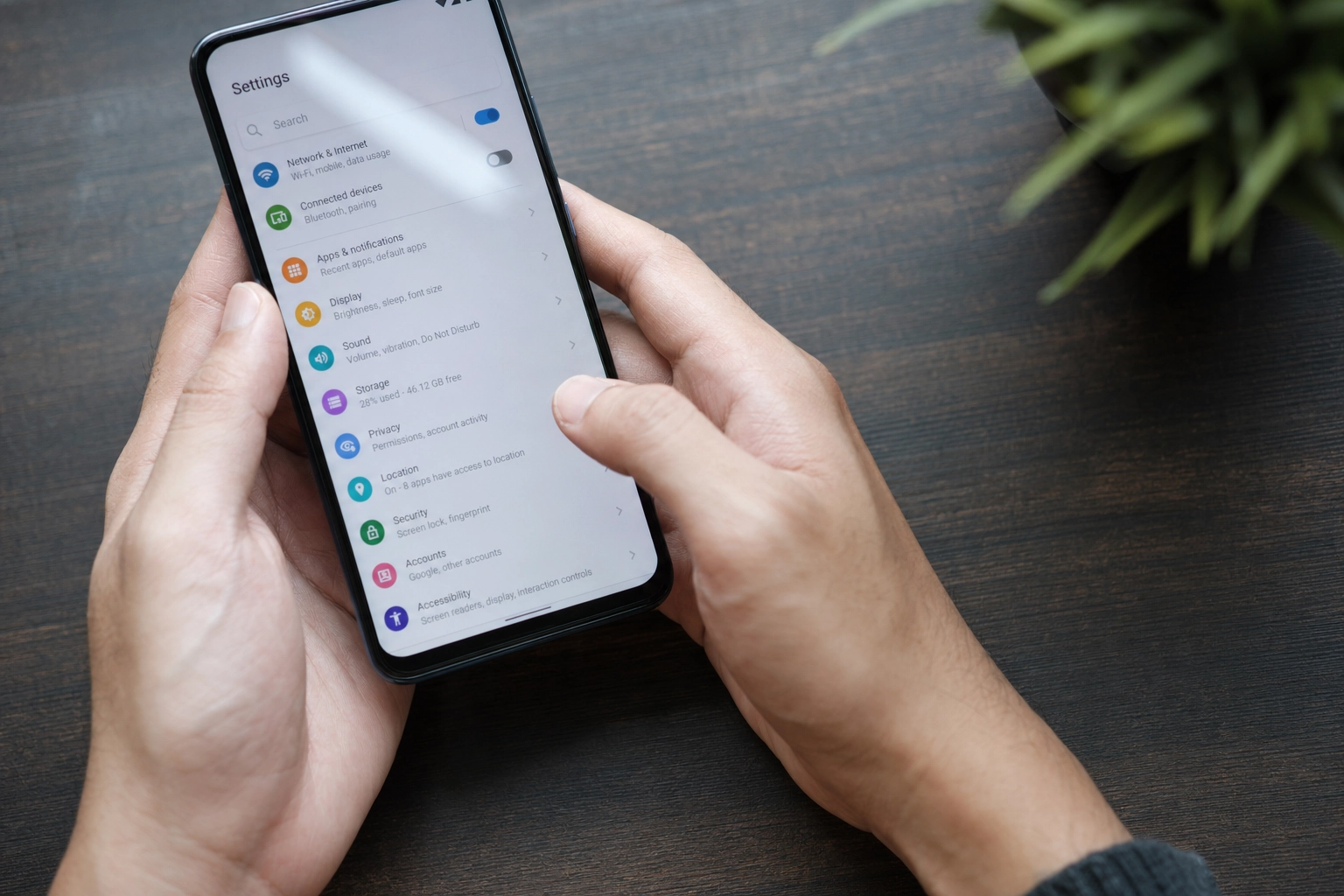 Hands holding a smartphone with the system language switched to English on a wooden desk