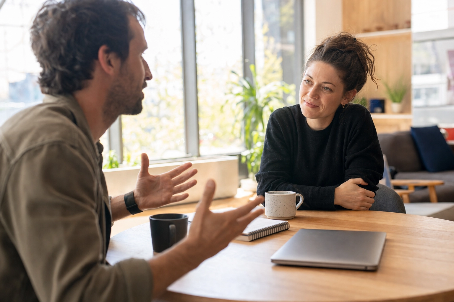 Two people having an animated unscripted English conversation at a sunlit co-working space