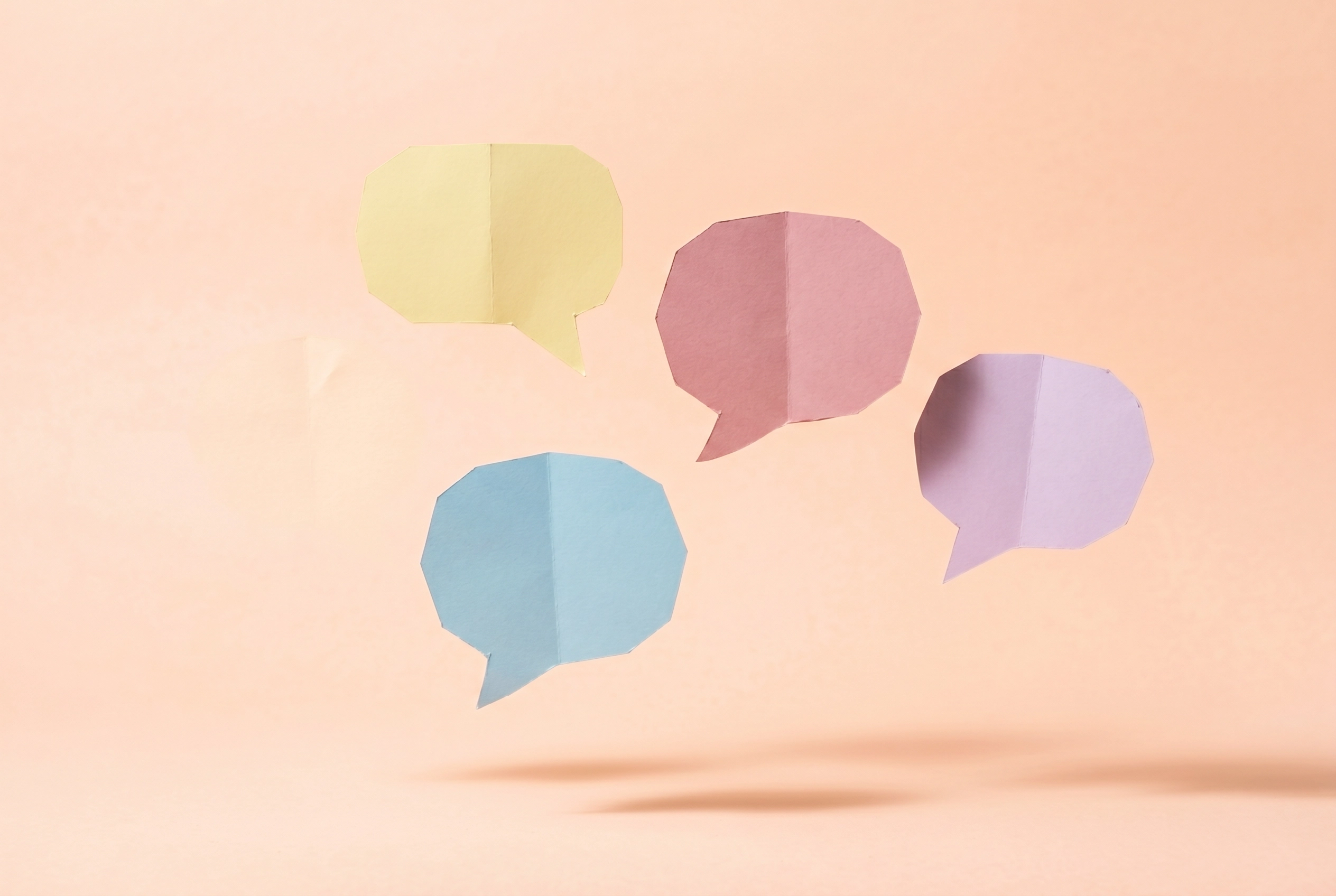 Balon percakapan kertas buatan tangan warna-warni melayang di latar persik melambangkan dialog pertanyaan yang sering diajukan tentang Gliglish